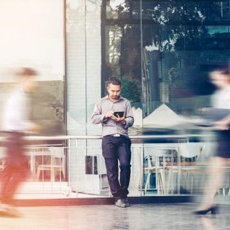 Businessman using a digital tablet office outdoors and Blurred People Walking in Front of Modern Office Building